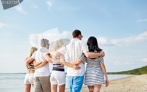 Image of smiling friends hugging and walking on beach