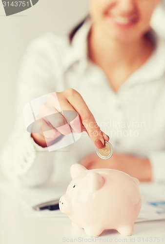 Image of woman hand putting coin into small piggy bank