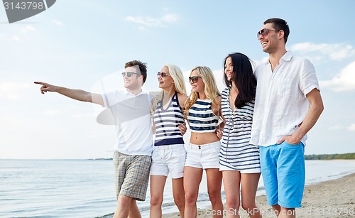 Image of smiling friends in sunglasses walking on beach
