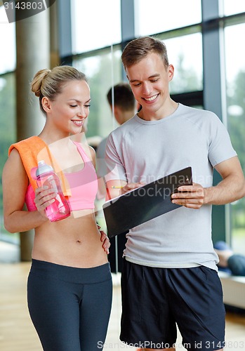 Image of smiling young woman with personal trainer in gym