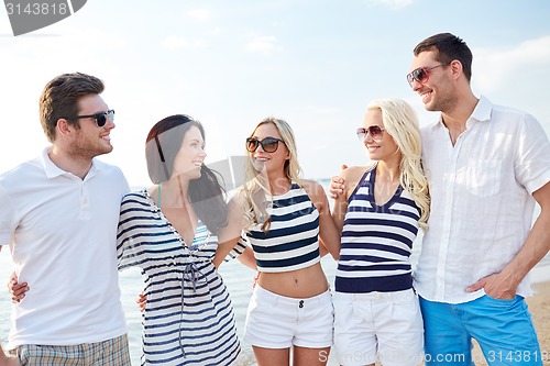 Image of smiling friends in sunglasses talking on beach