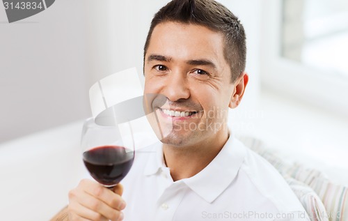 Image of happy man drinking red wine from glass at home