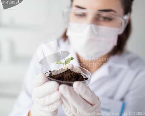 Image of close up of scientist with plant and soil in lab