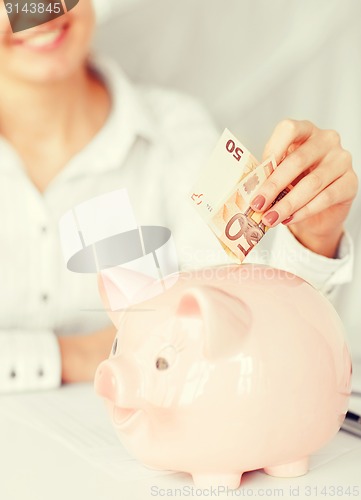 Image of woman puts euro cash into large piggy bank