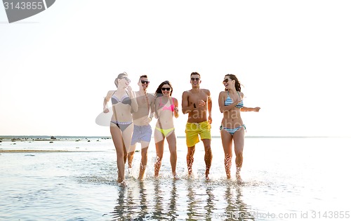 Image of smiling friends in sunglasses running on beach