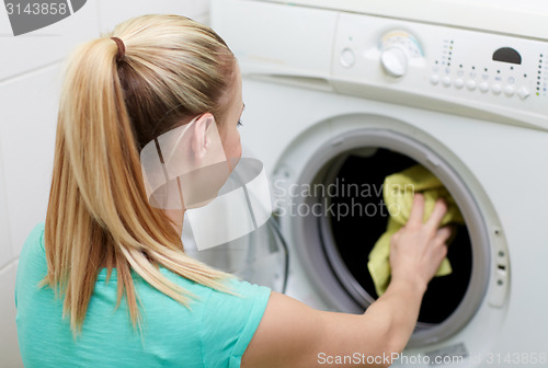 Image of happy woman putting laundry into washer at home