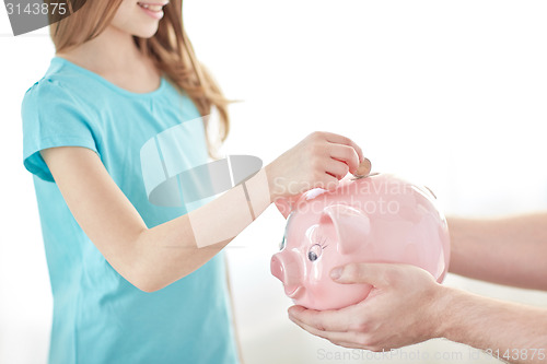 Image of close up of girl putting coin into piggy bank