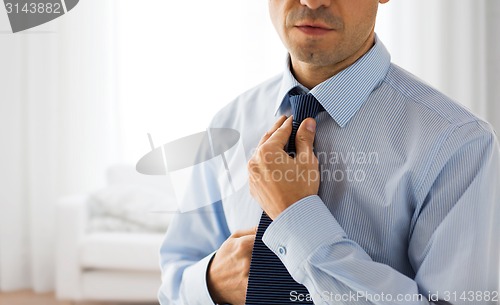 Image of close up of man in shirt adjusting tie on neck