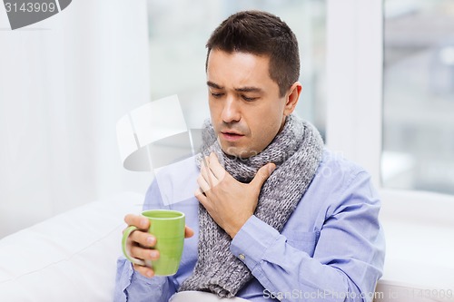 Image of ill man with flu drinking tea and coughing at home