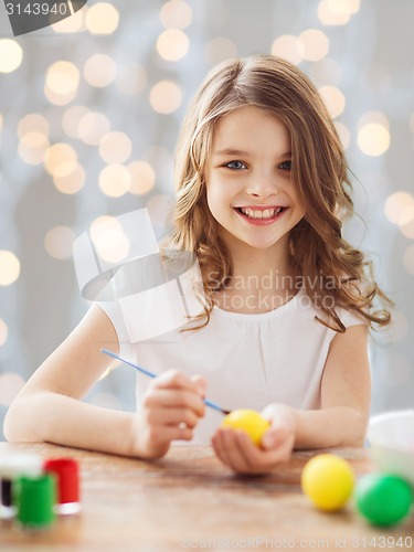 Image of close up of girl with brush coloring easter eggs