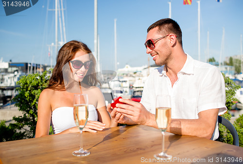 Image of smiling couple with champagne and gift at cafe