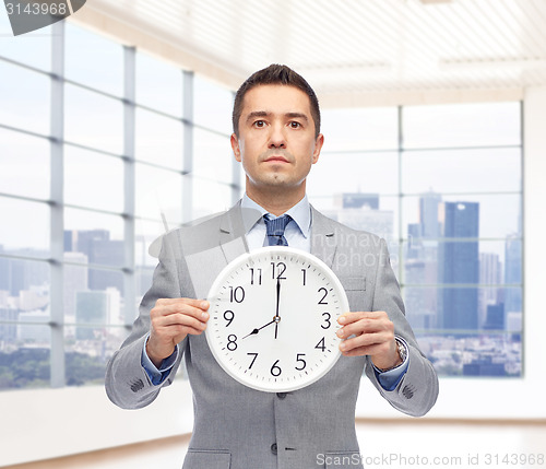 Image of businessman in suit holding clock with 8 o'clock