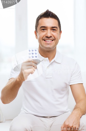 Image of happy man showing pack of pills at home