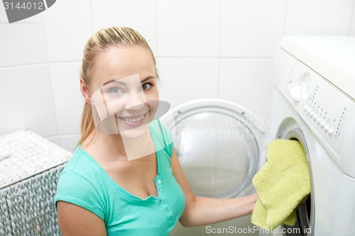 Image of happy woman putting laundry into washer at home