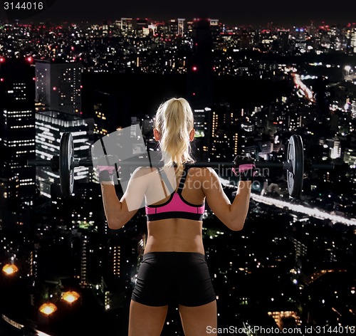 Image of sporty woman exercising with barbell from back