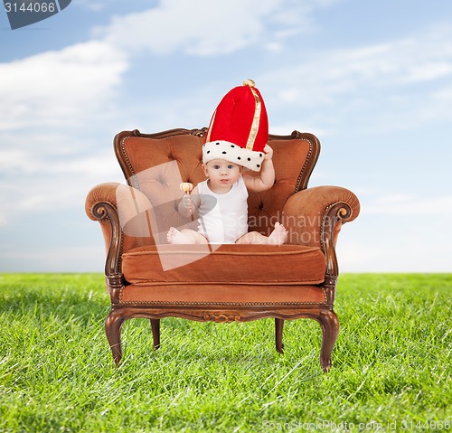 Image of baby in royal hat with lollipop sitting on chair