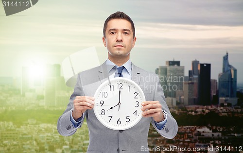 Image of businessman in suit holding clock with 8 o'clock