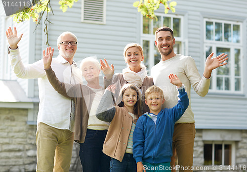 Image of happy family waving hands in front of house