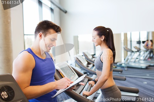 Image of happy woman with trainer on treadmill in gym