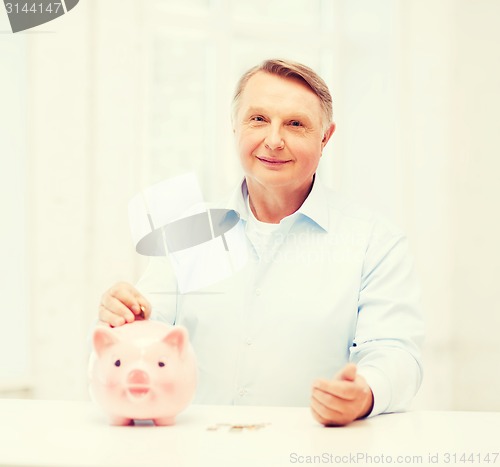 Image of old man putting coin into big piggy bank