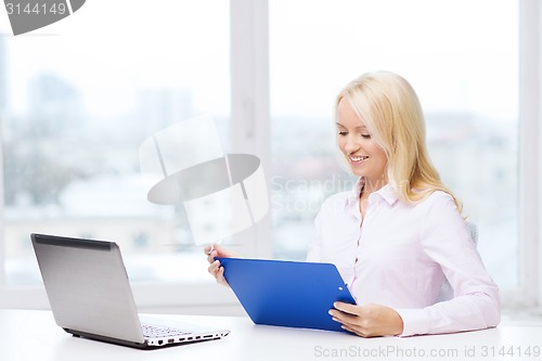 Image of smiling businesswoman reading papers in office