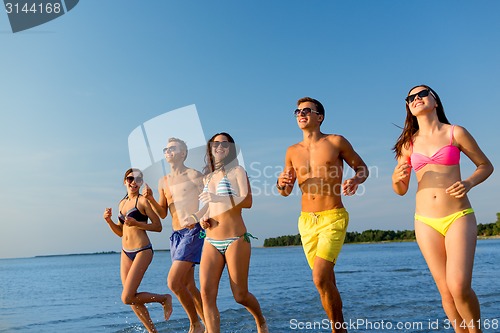 Image of smiling friends in sunglasses running on beach