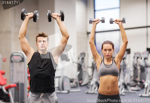 Image of smiling man and woman with dumbbells in gym