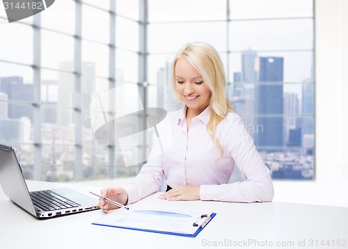 Image of smiling businesswoman reading papers in office