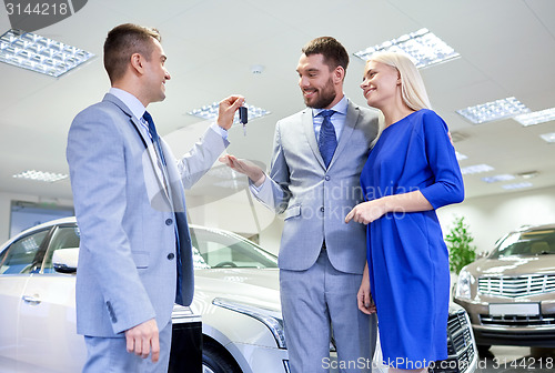 Image of happy couple with car dealer in auto show or salon