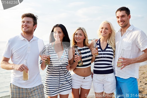 Image of smiling friends with drinks in bottles on beach