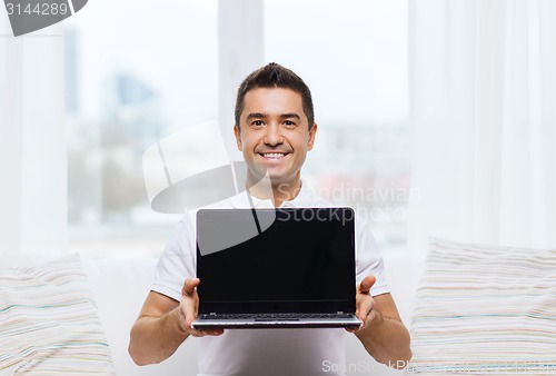 Image of happy man showing laptop blank screen at home
