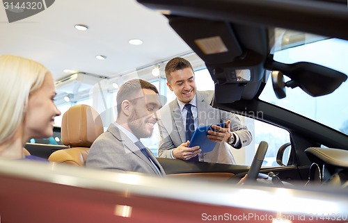 Image of happy couple with car dealer in auto show or salon