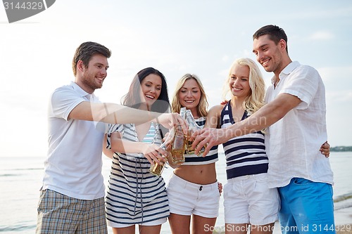 Image of smiling friends clinking bottles on beach