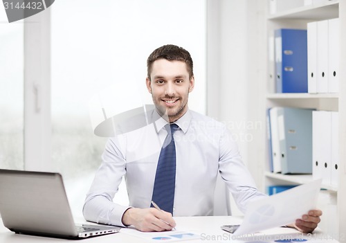 Image of smiling businessman with laptop and documents