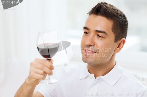 Image of happy man drinking red wine from glass at home