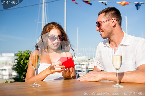 Image of smiling couple with champagne and gift at cafe