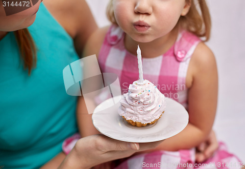 Image of happy mother and girl blowing out cupcake candle