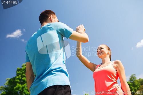 Image of two smiling people making high five outdoors