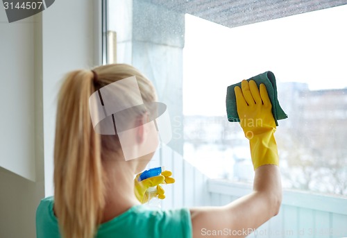 Image of happy woman in gloves cleaning window with rag