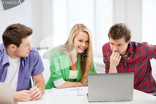 Image of smiling students looking at laptop at school