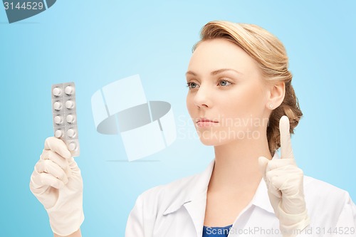 Image of young female doctor with pills pointing finger up