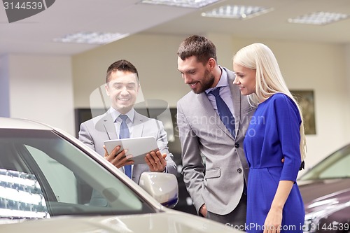 Image of happy couple with car dealer in auto show or salon