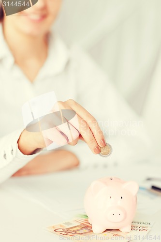 Image of woman hand putting coin into small piggy bank