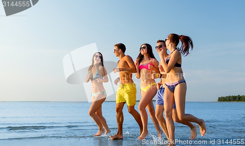 Image of smiling friends in sunglasses running on beach