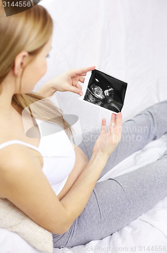 Image of happy pregnant woman with ultrasound image at home