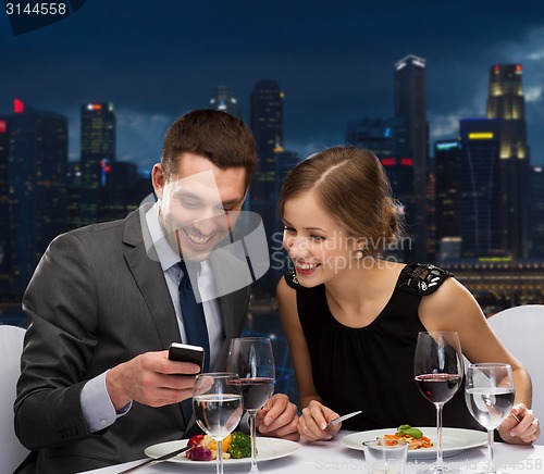 Image of smiling couple with smartphone at restaurant