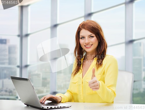 Image of smiling young woman with laptop showing thumbs up