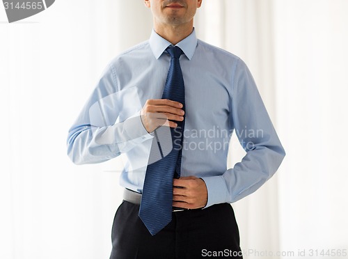 Image of close up of man in shirt adjusting tie on neck