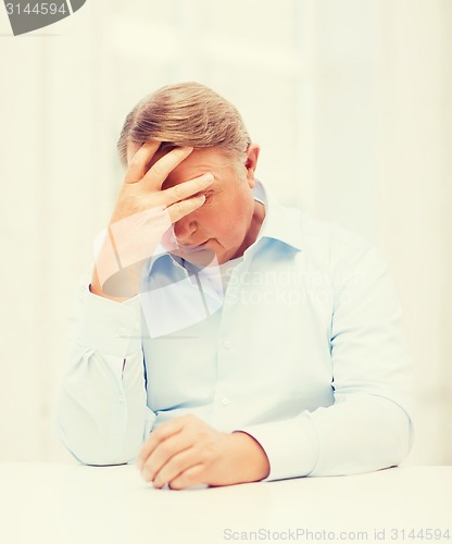 Image of stressed old man holding head at home