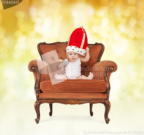 Image of baby in royal hat with lollipop sitting on chair